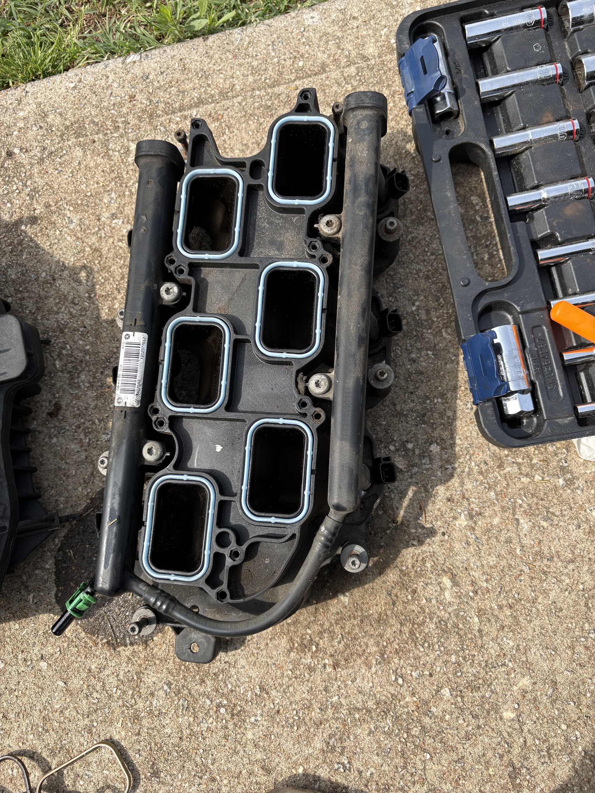 An intake manifold laid on concrete next to a socket set